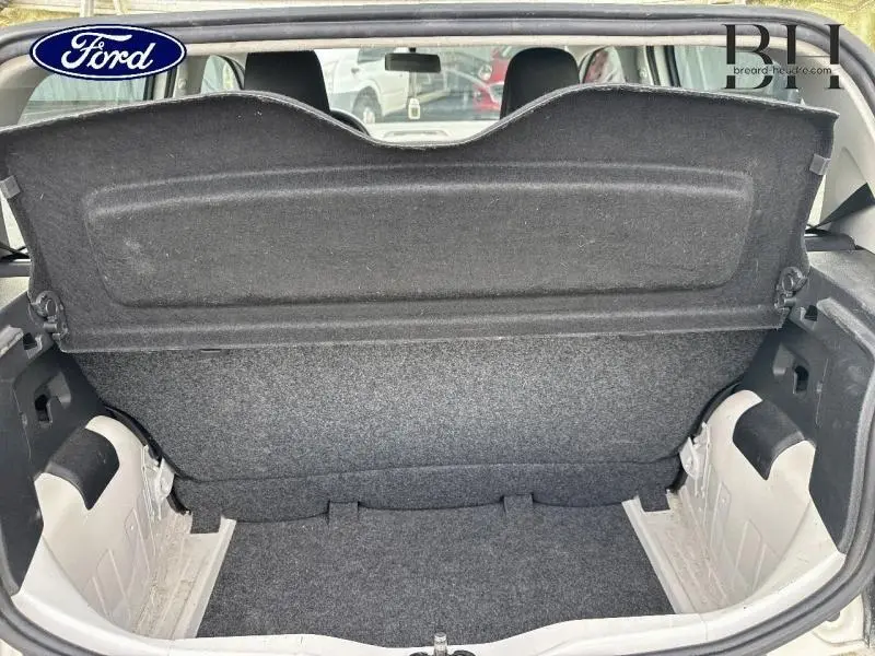 Coffre ouvert vu de l'arrière d'une Volkswagen Up blanche, montrant la plage arrière et l'espace de chargement vide.