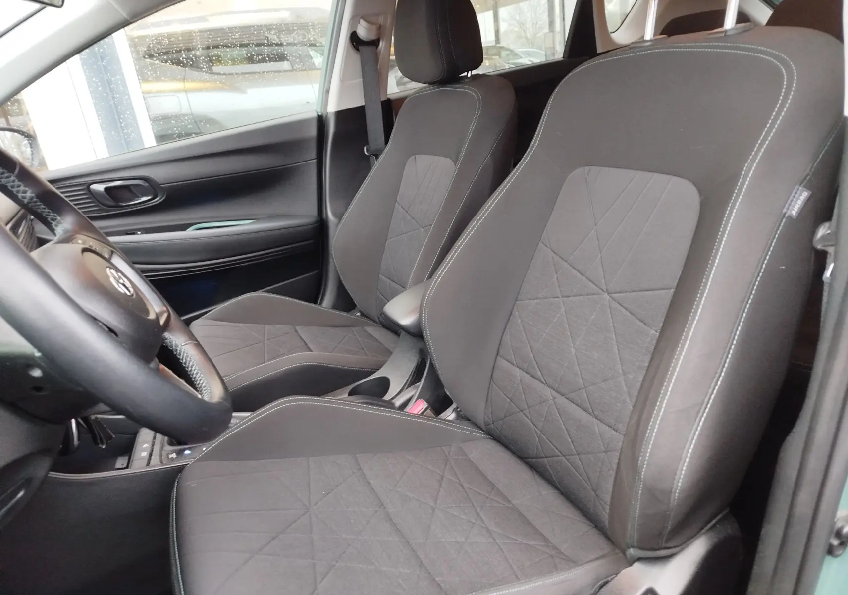 Vue intérieure côté gauche des sièges avant noirs avec surpiqûres blanches du Hyundai Bayon 2022 hybride en couleur Elemental Brass Metal.