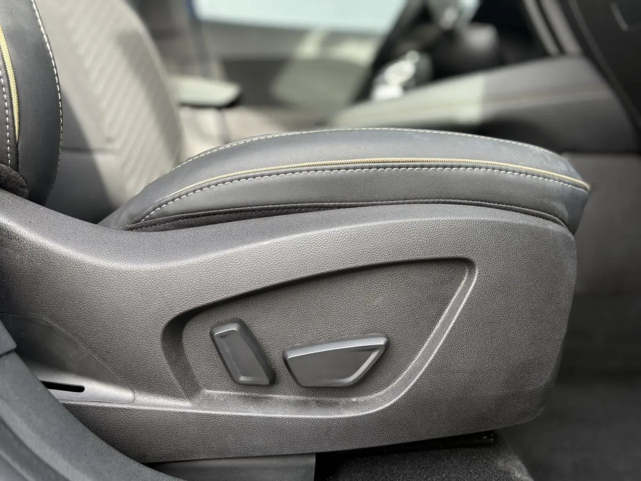 Gros plan sur les commandes de réglage électrique du siège avant droit en cuir noir avec surpiqûres jaunes du Renault Symbioz.