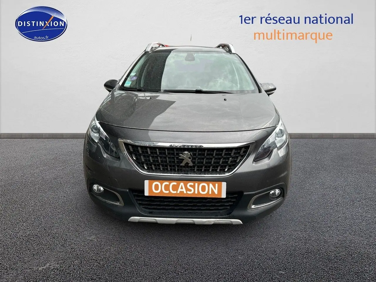 Vue frontale d'un Peugeot 2008 gris platinium de 2019 avec calandre noire et phares allumés sur fond neutre.