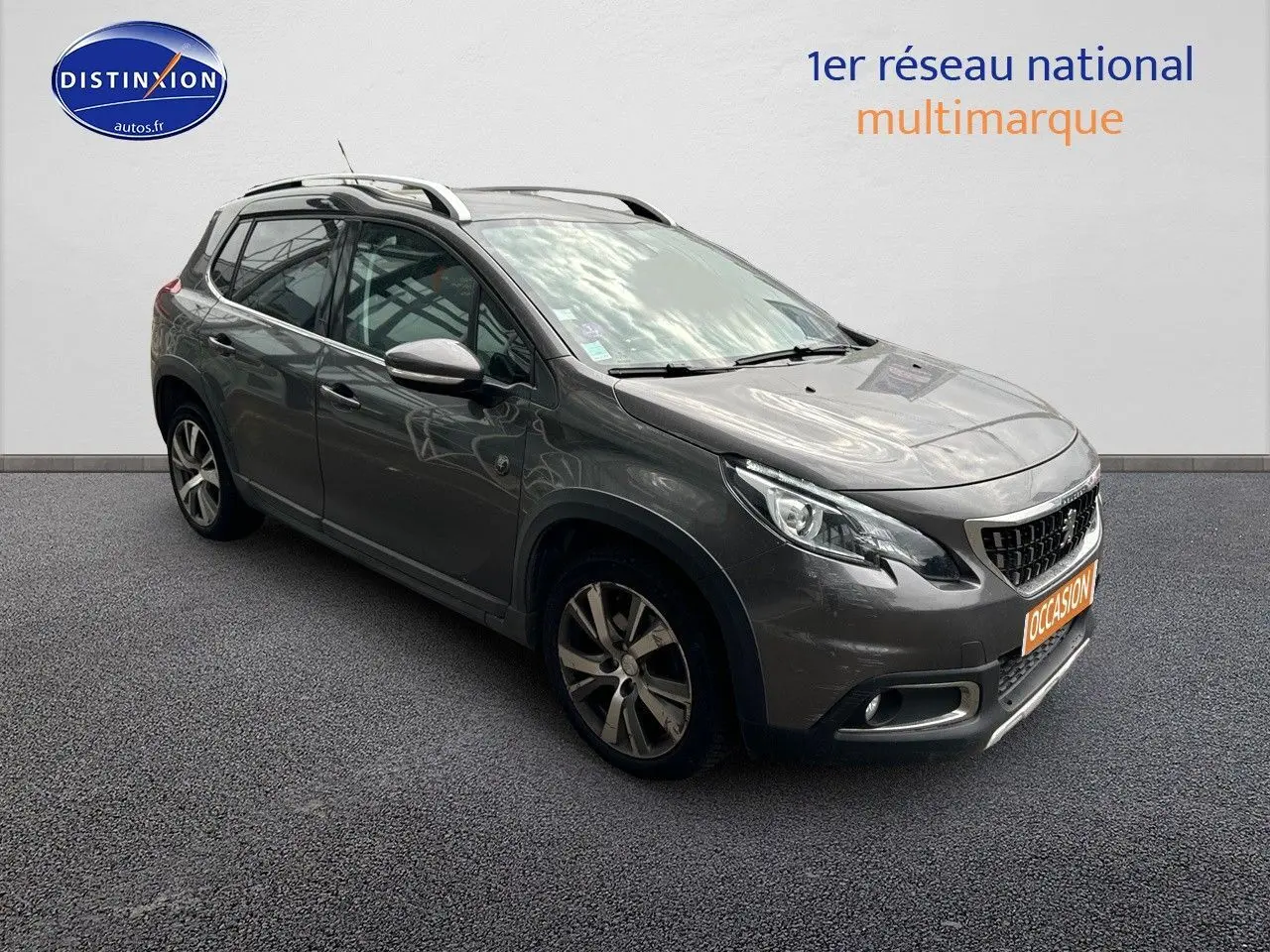 Peugeot 2008 gris platinium en 3/4 avant droit, avec jantes alliage et barres de toit visibles.