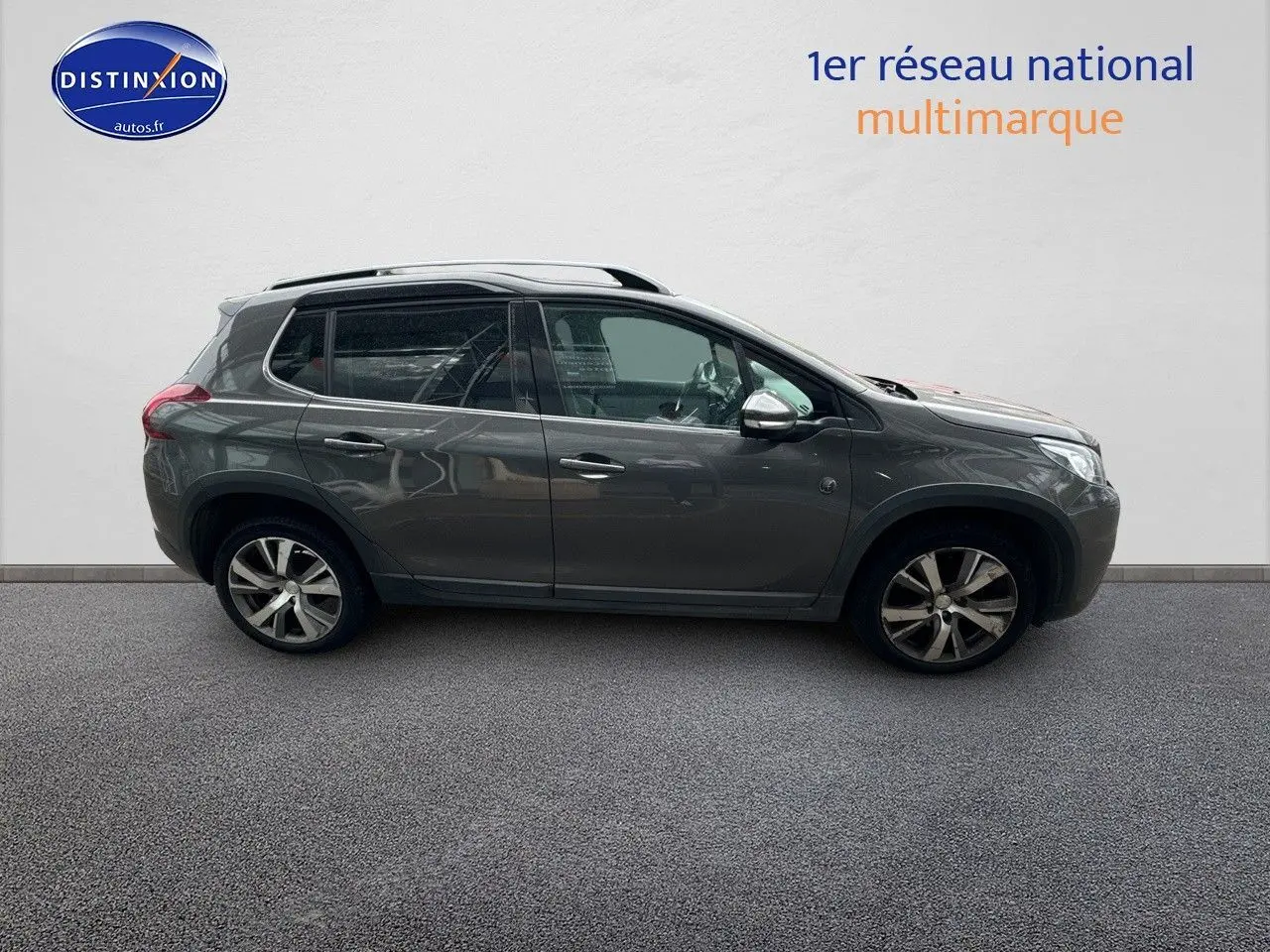 Profil côté gauche d'un Peugeot 2008 gris platinium de 2019 avec jantes alliage et barres de toit visibles.