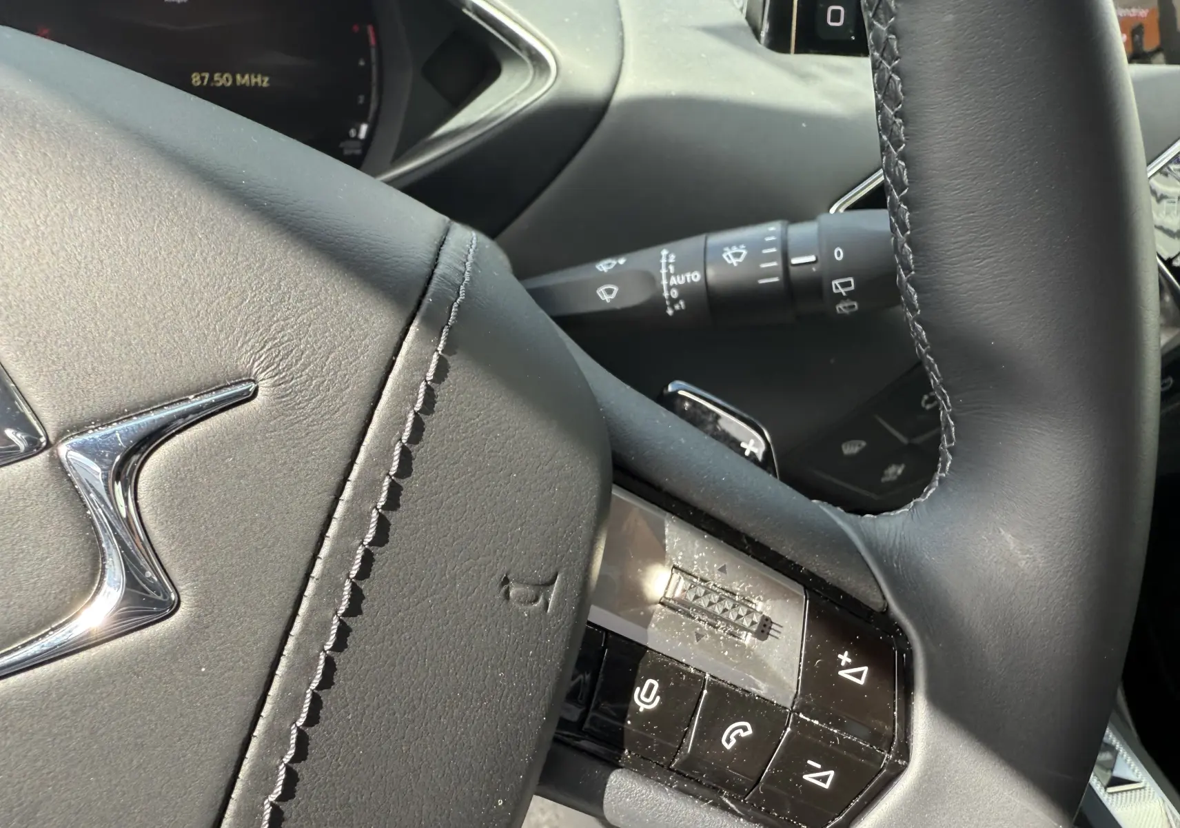 Gros plan sur le volant en cuir noir du DS3 2024, avec commandes intégrées et logo DS chromé visible.