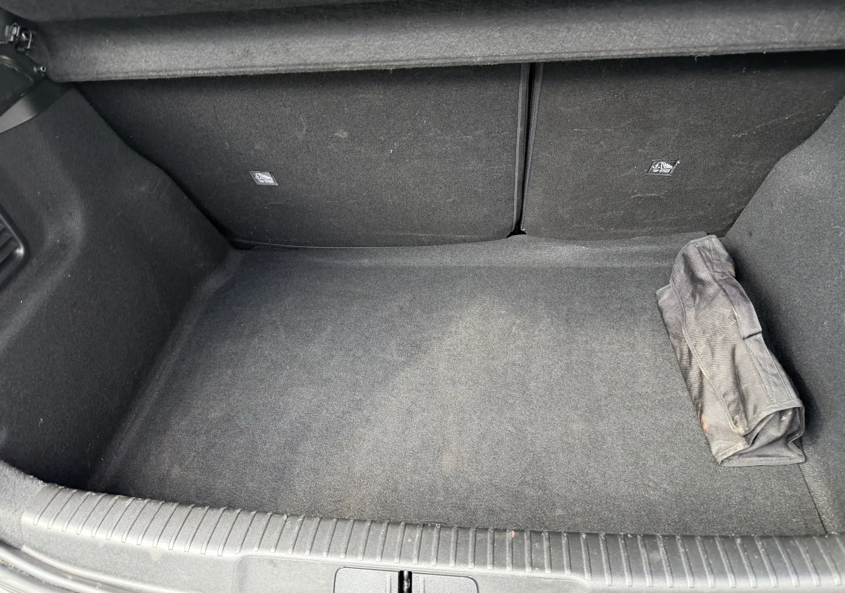Coffre spacieux et propre du DS3 2024 gris laqué, avec un sac noir roulé posé à droite.
