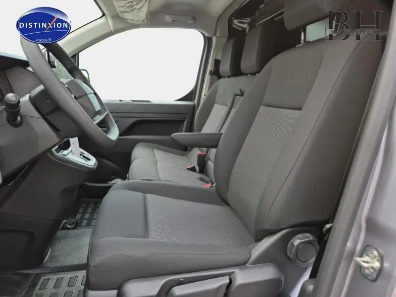 Vue intérieure côté conducteur du Citroën Jumpy Fourgon gris acier métal, sièges tissu bi-ton noir et gris avec accoudoir central.