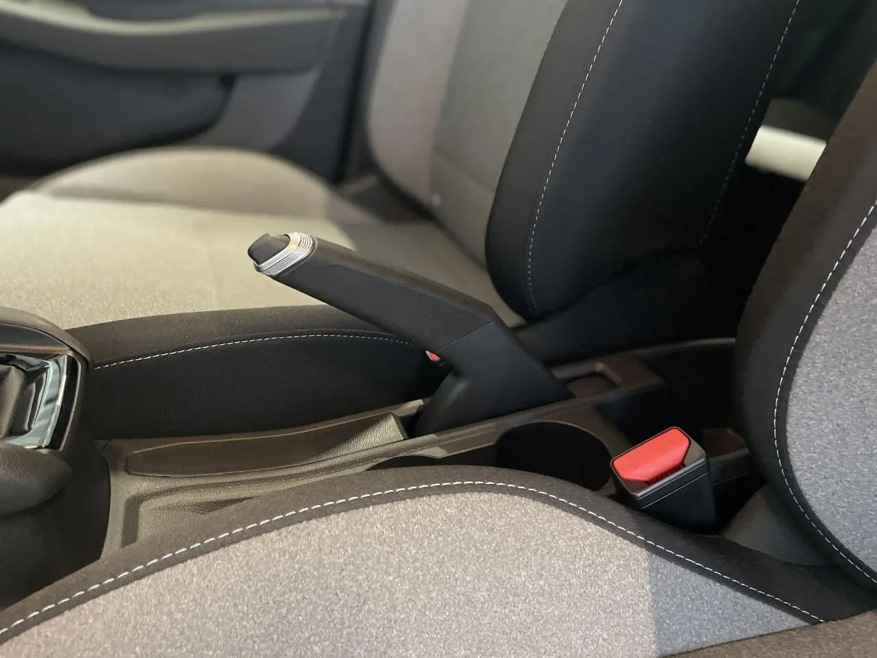 Gros plan sur frein à main manuel et ceinture rouge entre sièges tissu gris et noir d'une Renault Clio 2025.