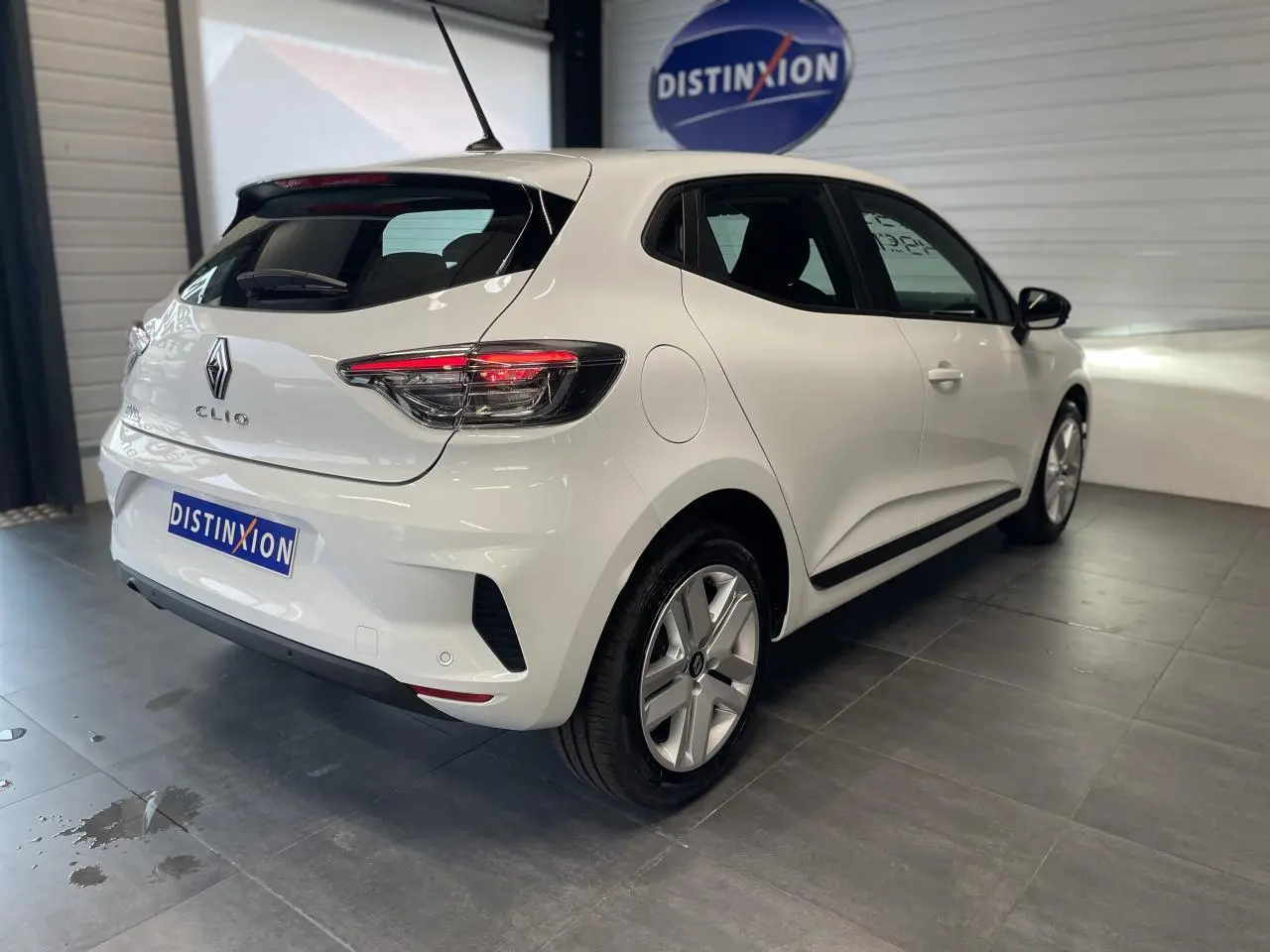 Vue 3/4 arrière droite d'une Renault Clio blanche avec feux LED et jantes alliage dans un showroom.