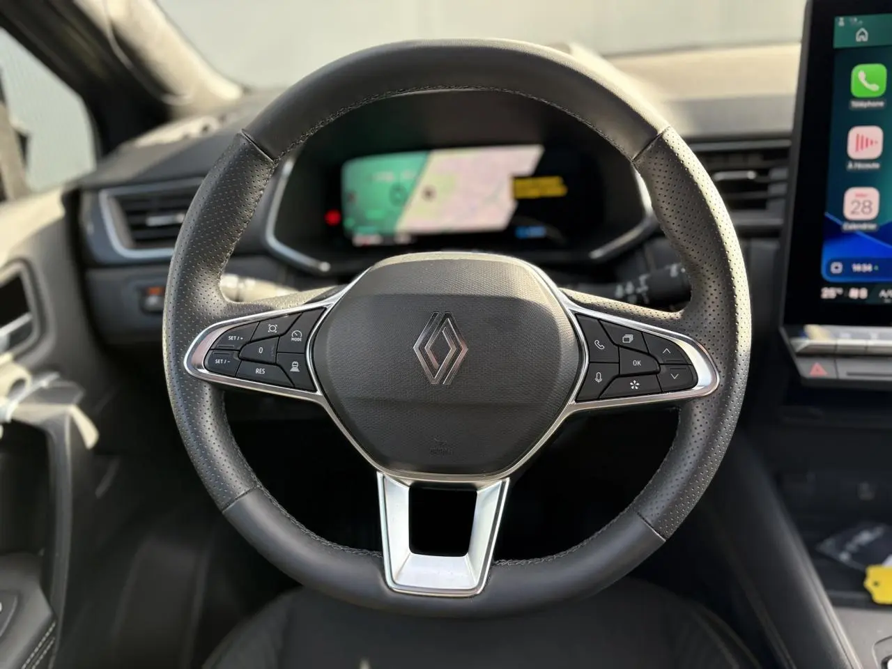 Vue rapprochée du volant en cuir noir perforé avec logo Renault, tableau de bord numérique et écran tactile à droite.