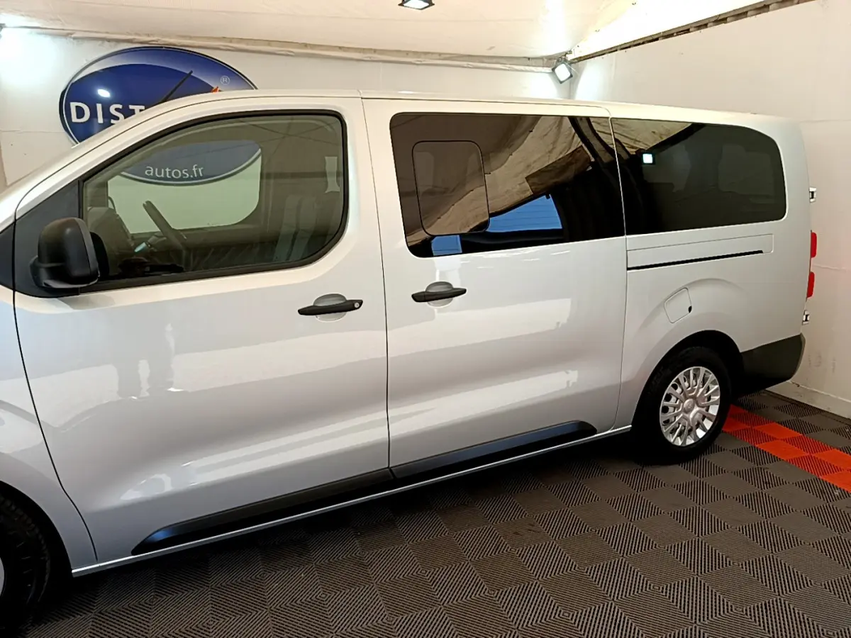 Vue latérale droite d'un Toyota Proace Verso gris clair avec vitres arrière teintées dans un intérieur fermé.