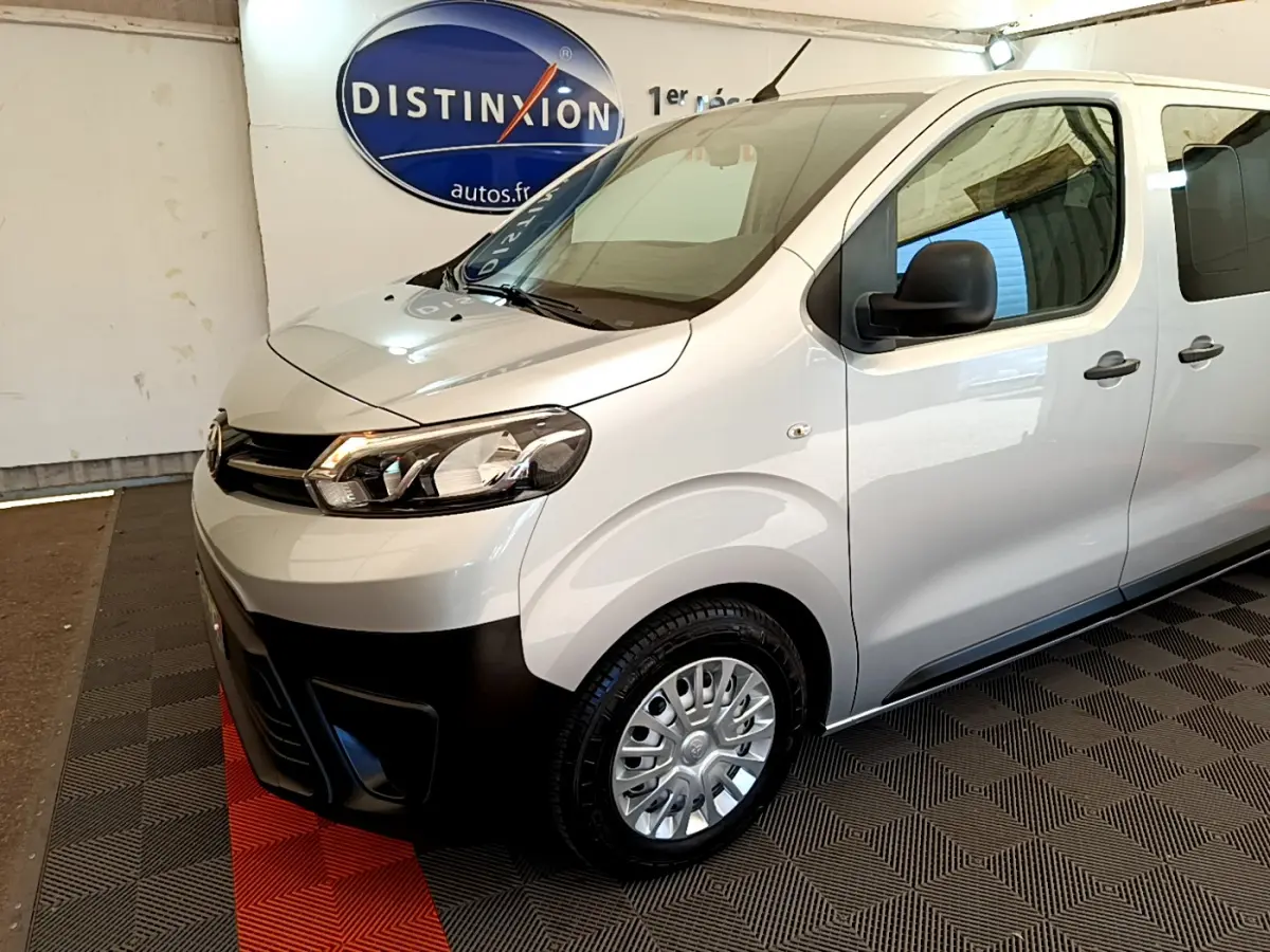 Vue 3/4 avant droit du Toyota Proace Verso gris clair avec pare-chocs noir et jantes acier en intérieur showroom.