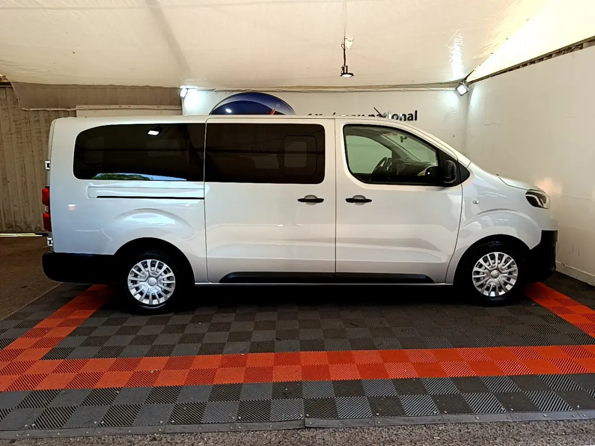 Profil côté droit d'un Toyota Proace Verso gris clair 2019 avec vitres arrière teintées et jantes acier en intérieur fermé.