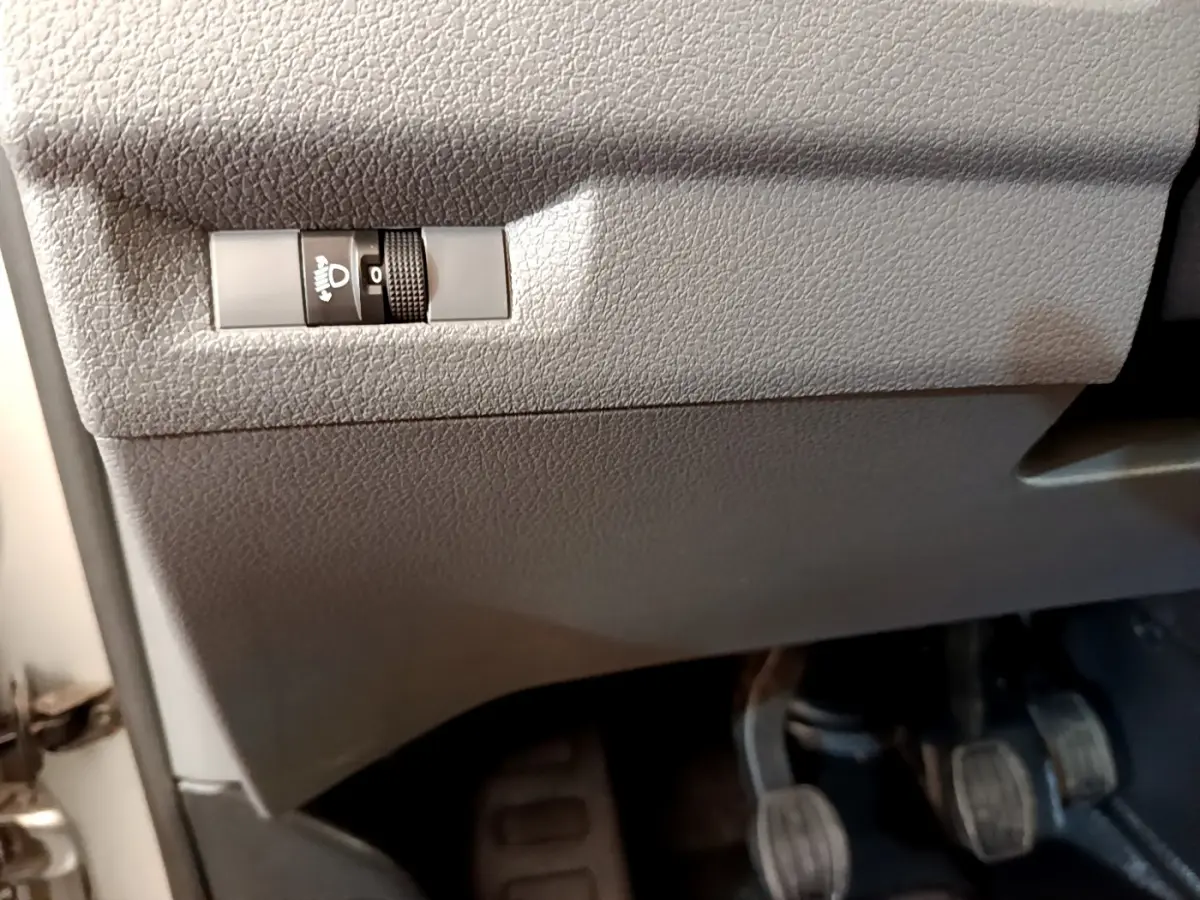 Gros plan sur le réglage manuel en hauteur des phares sous le tableau de bord gris clair du Toyota Proace Verso 2019.
