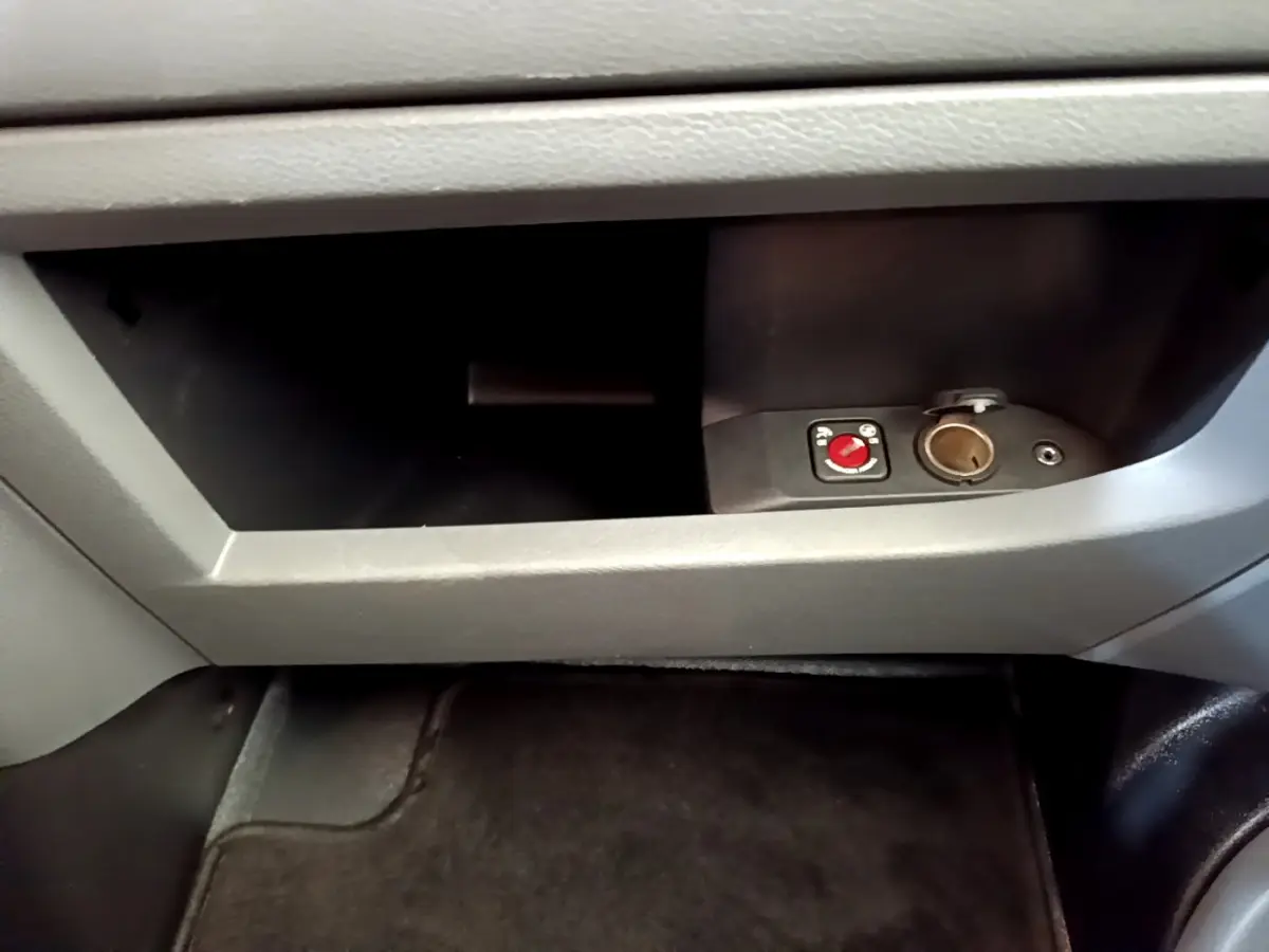 Gros plan sur la boîte à gants grise du Toyota Proace Verso 2019 avec prise 12V et commande rouge visible.