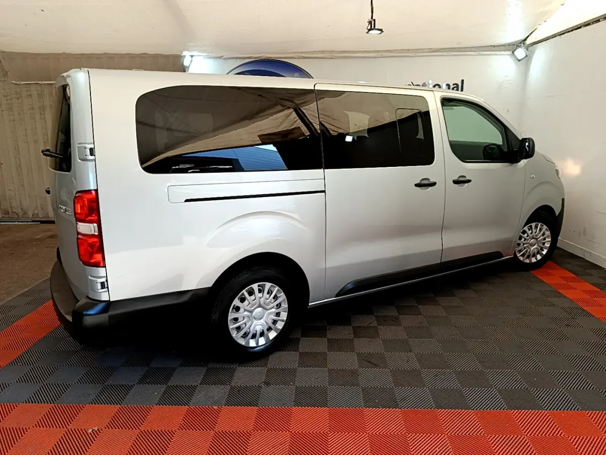 Vue 3/4 arrière droite du Toyota Proace Verso gris clair avec vitres teintées et jantes acier en intérieur showroom.