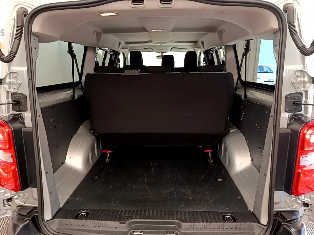 Vue arrière du coffre ouvert d'un Toyota Proace Verso gris clair, montrant la banquette arrière noire et l'espace de chargement vide.
