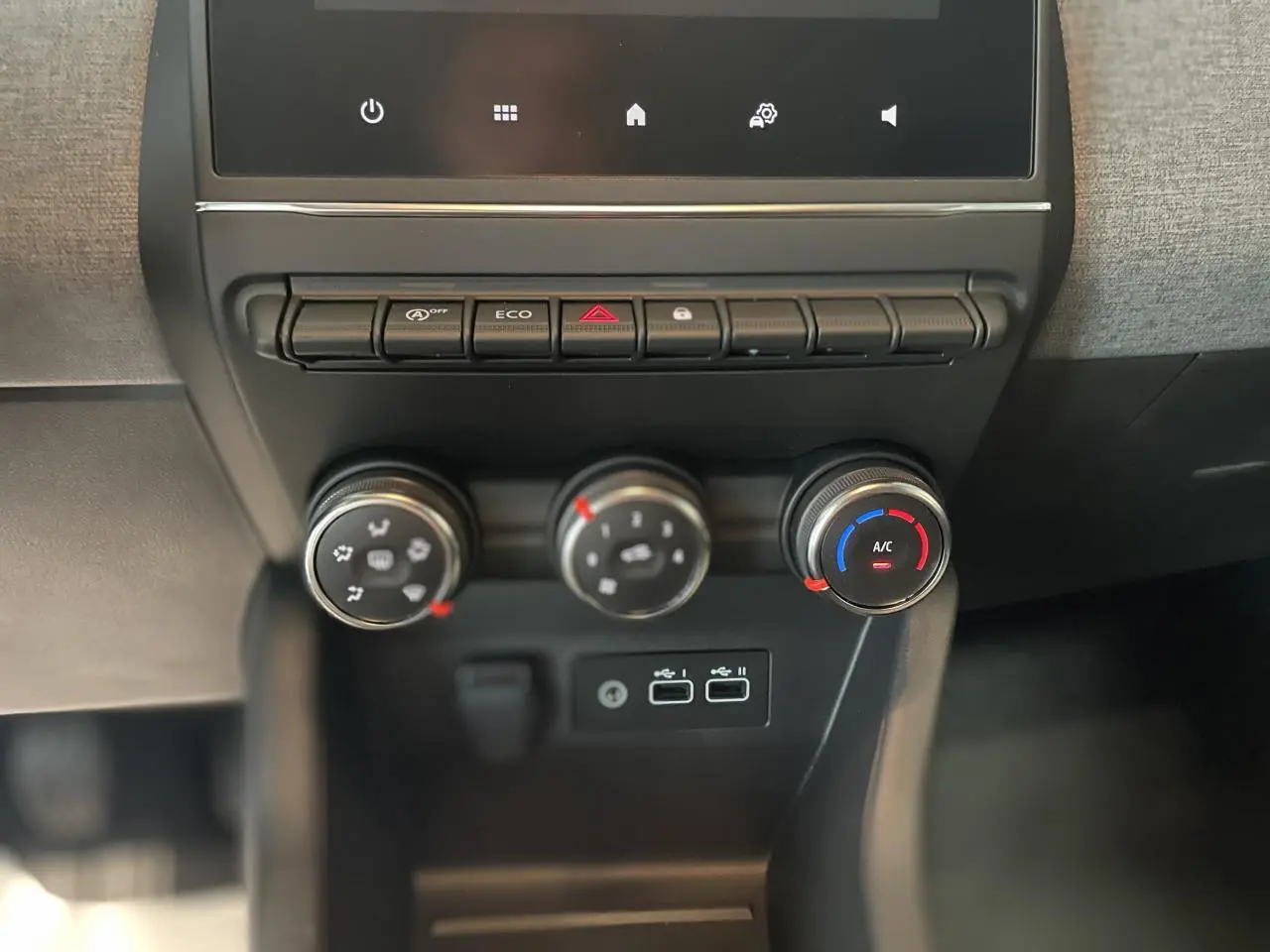 Gros plan sur la console centrale de la Renault Clio 2025 blanche, montrant les commandes de climatisation et les ports USB.