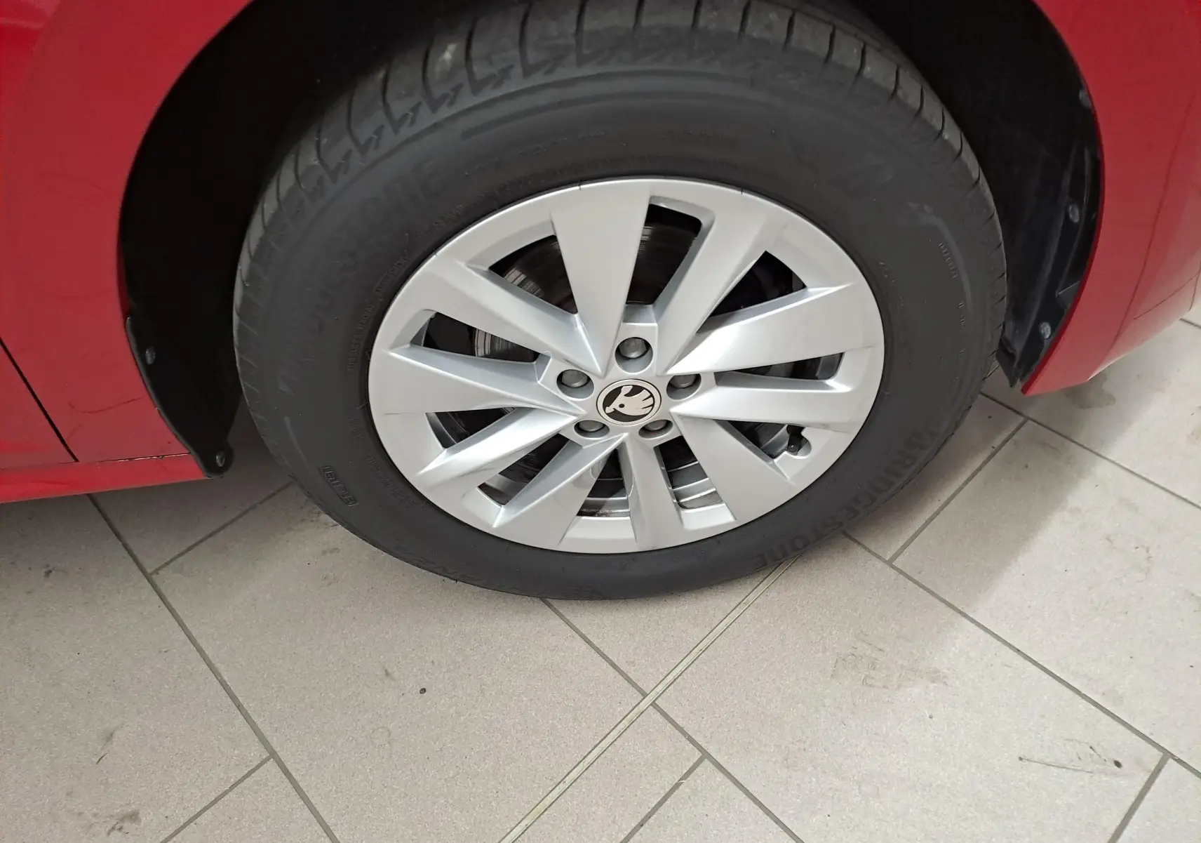 Gros plan sur la roue avant gauche d'un Skoda Kamiq rouge Velvet avec jante alliage et logo central visible.