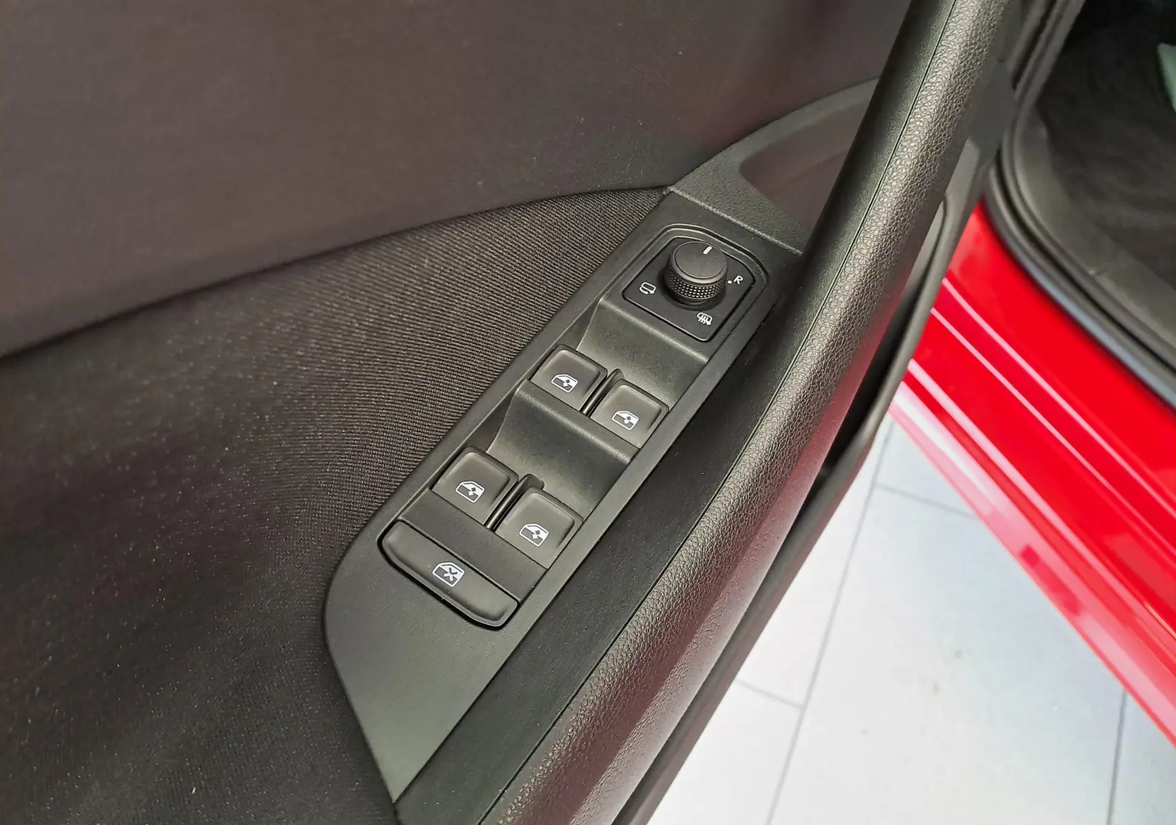 Commande des vitres et réglage des rétroviseurs côté conducteur sur la porte rouge métallisée d'un Skoda Kamiq 2024.