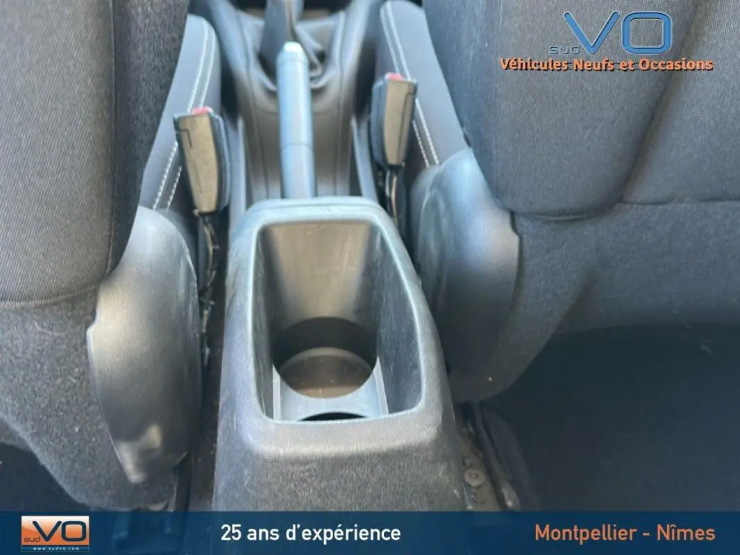 Gros plan sur la console centrale et le frein à main entre les sièges avant noirs d'une Peugeot 208 blanche de 2015.