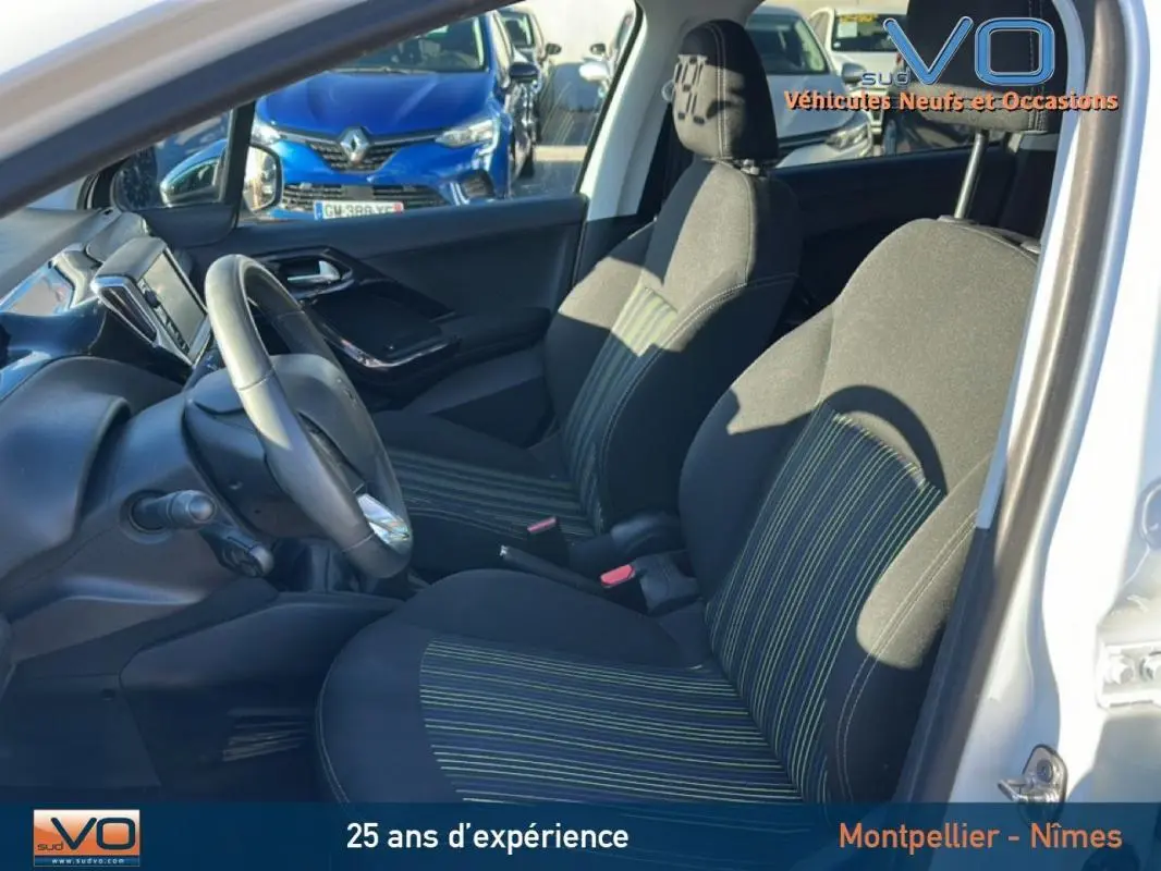 Vue intérieure côté conducteur de la Peugeot 208 blanche de 2015, sièges noirs à rayures vertes et volant visible.