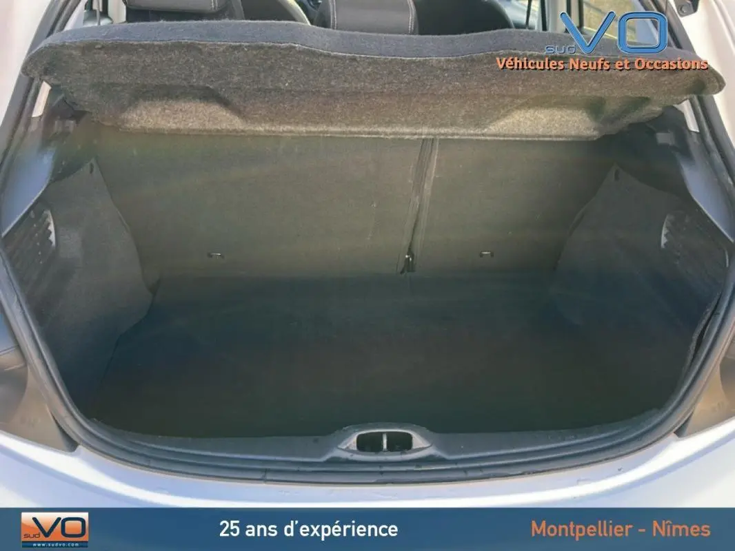 Coffre ouvert d'une Peugeot 208 blanche vue de l'arrière, montrant l'espace de chargement vide et la plage arrière relevée.