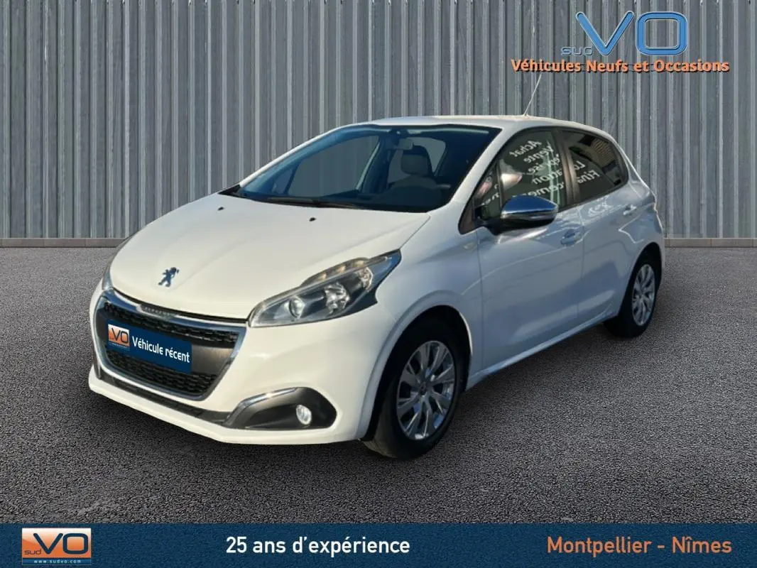 Peugeot 208 blanc vue 3/4 avant droit, avec jantes classiques 15 pouces et phares antibrouillard visibles.