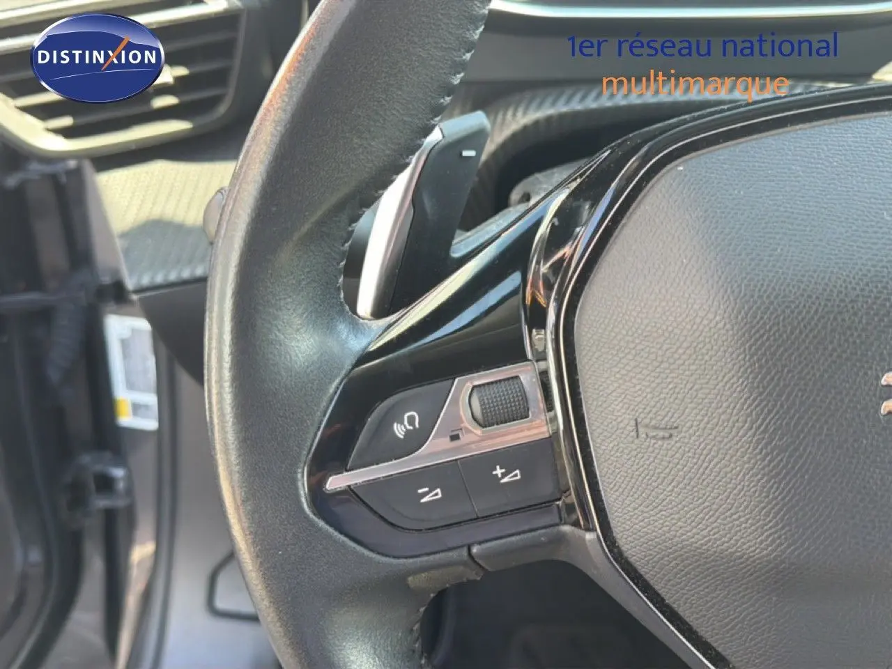 Gros plan sur le volant noir de la Peugeot 2008 1.2 PureTech 130, montrant les commandes audio et de volume.