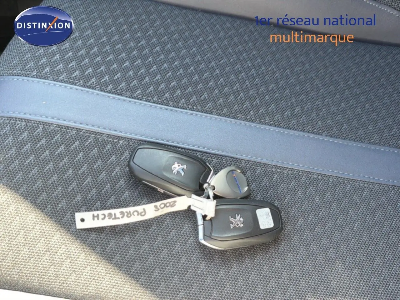 Clé de voiture Peugeot 2008 posée sur un siège tissu gris avec surpiqûre bleue, vue en gros plan.