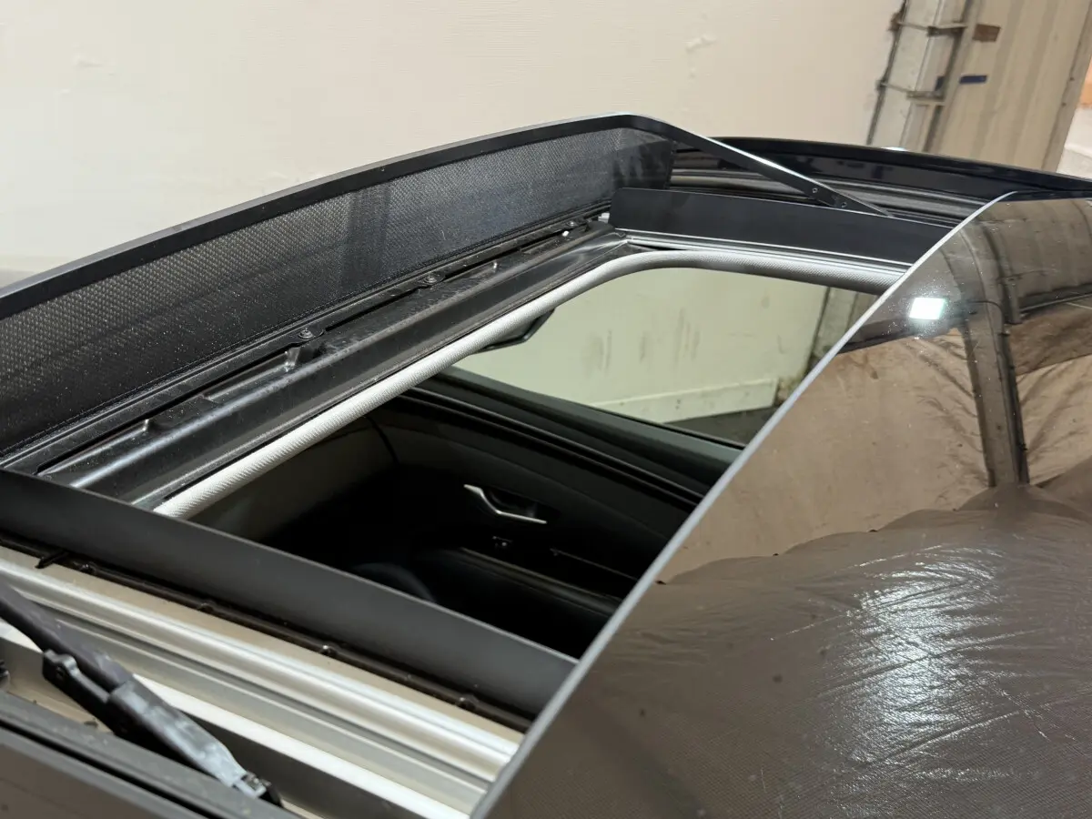 Toit ouvrant panoramique ouvert sur Hyundai Tucson noir, vue rapprochée sur l'ouverture et l'intérieur côté conducteur.