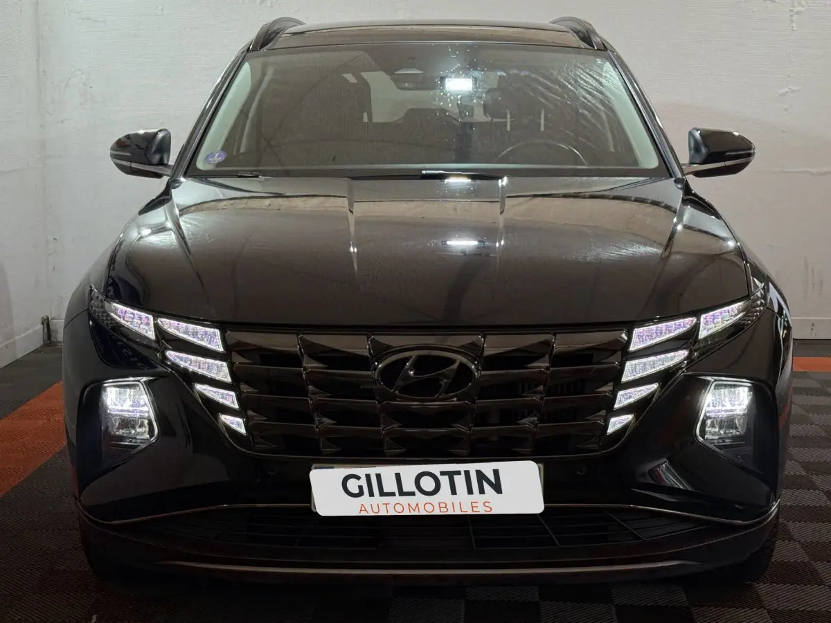 Vue frontale d'un Hyundai Tucson noir avec phares LED allumés et calandre imposante en intérieur showroom.