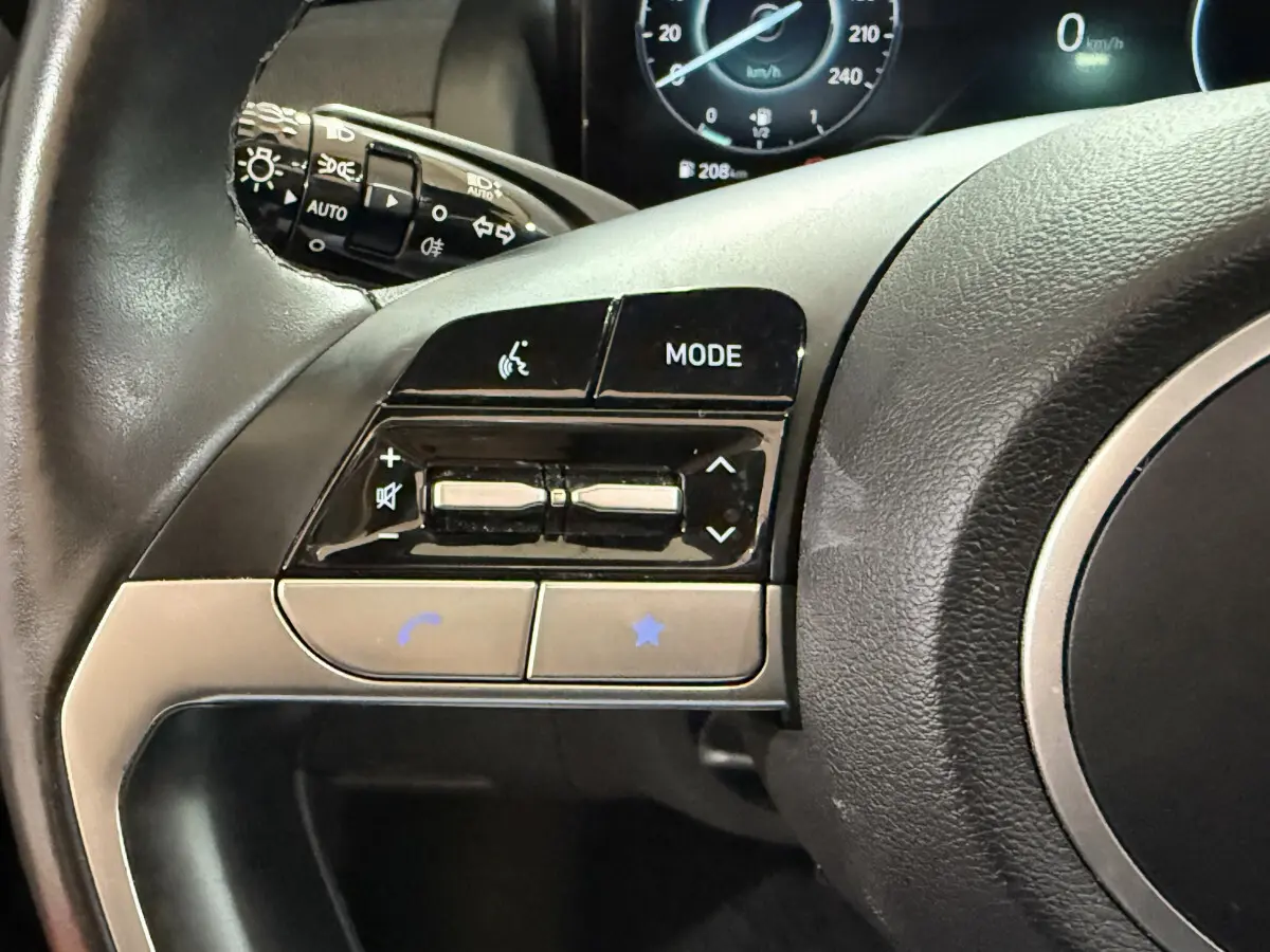 Gros plan sur les commandes gauche du volant noir du Hyundai Tucson 2021, avec tableau de bord numérique en arrière-plan.