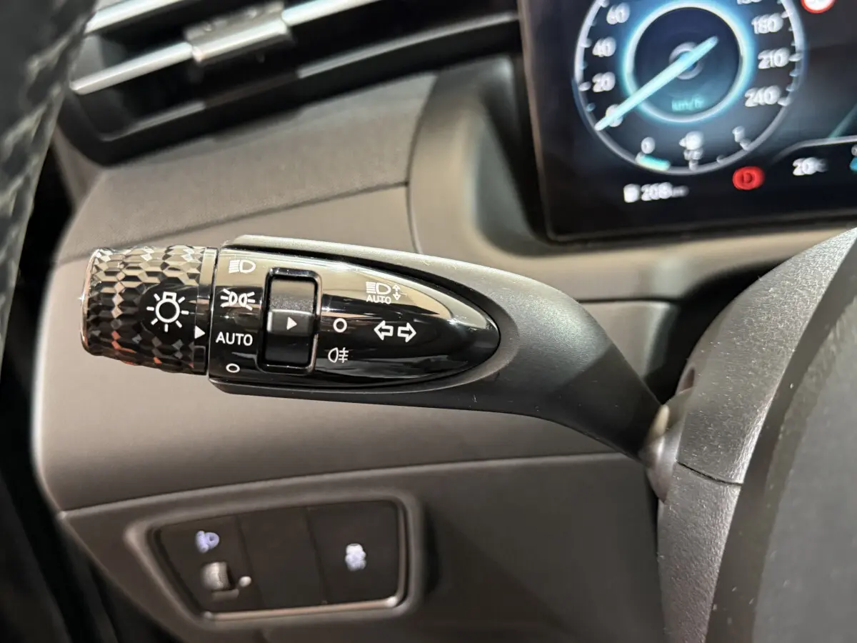 Gros plan sur la commande des phares et clignotants du Hyundai Tucson 2021, avec tableau de bord numérique en arrière-plan.