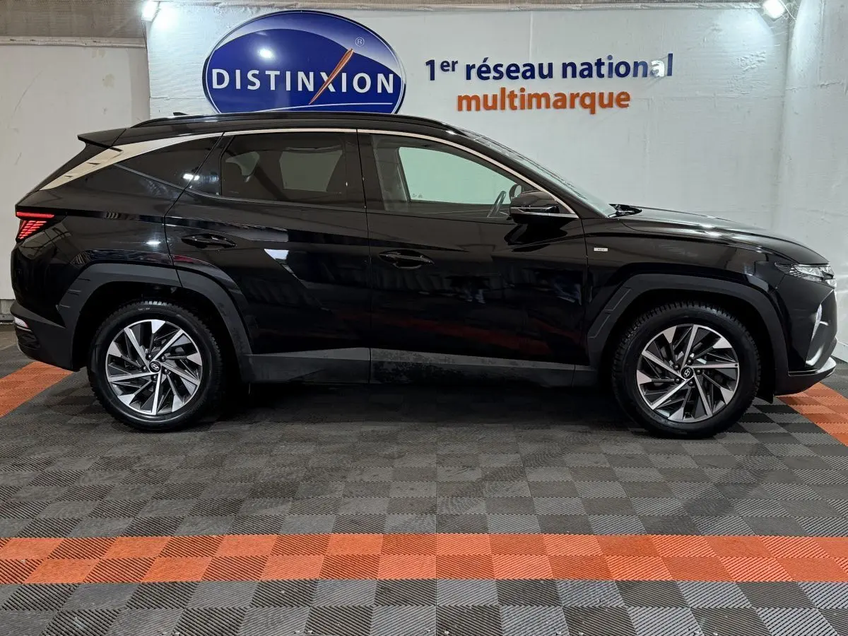 Profil côté gauche du Hyundai Tucson noir 2021 avec jantes alliage et lignes anguleuses modernes, en intérieur showroom.