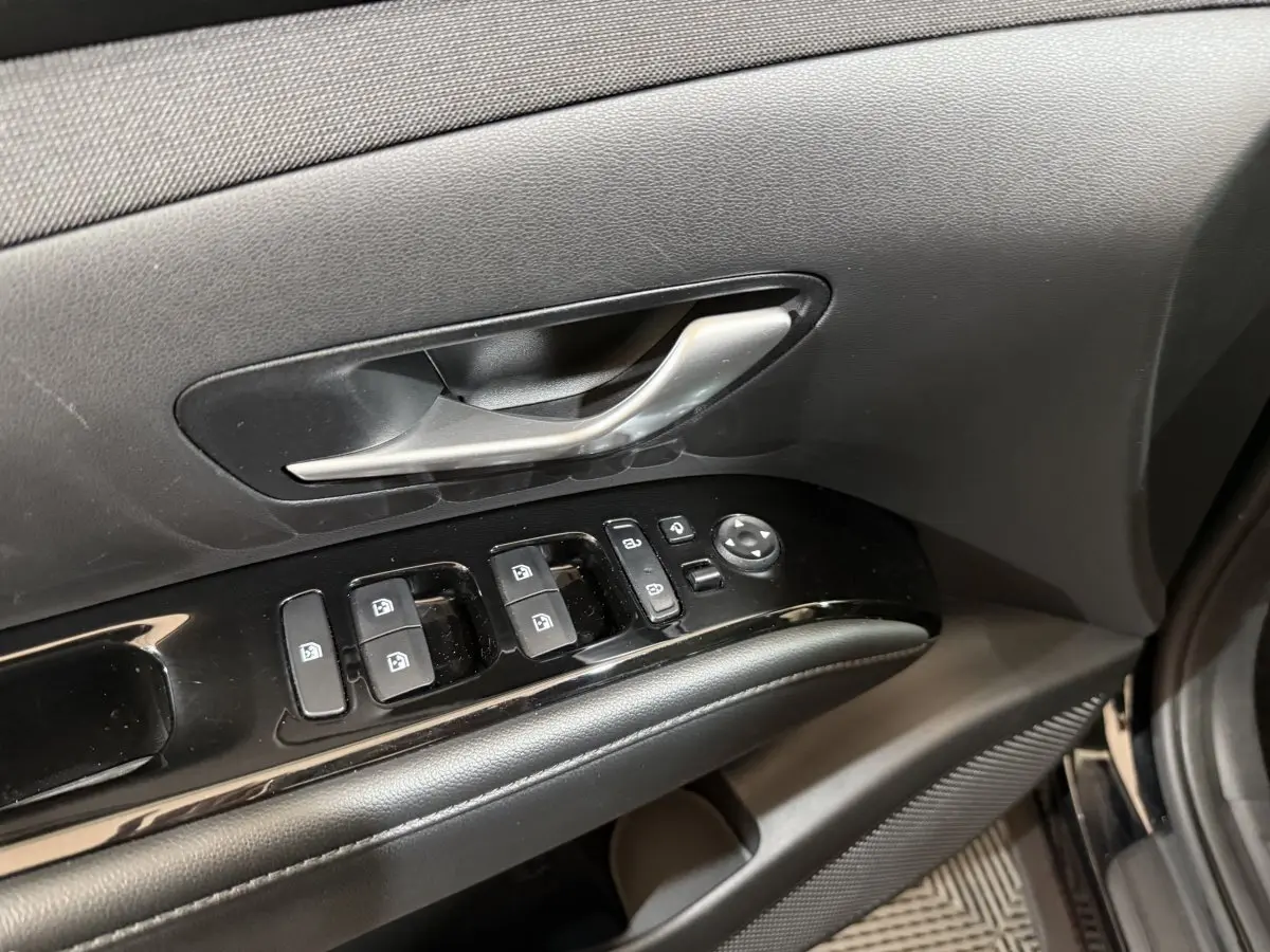 Gros plan sur la porte côté conducteur du Hyundai Tucson noir 2021, montrant les commandes des vitres et la poignée intérieure argentée.