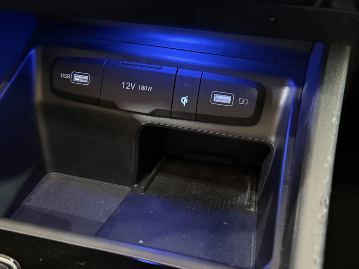 Gros plan sur la console centrale noire du Hyundai Tucson 2021 avec ports USB, prise 12V et chargeur à induction éclairés en bleu.