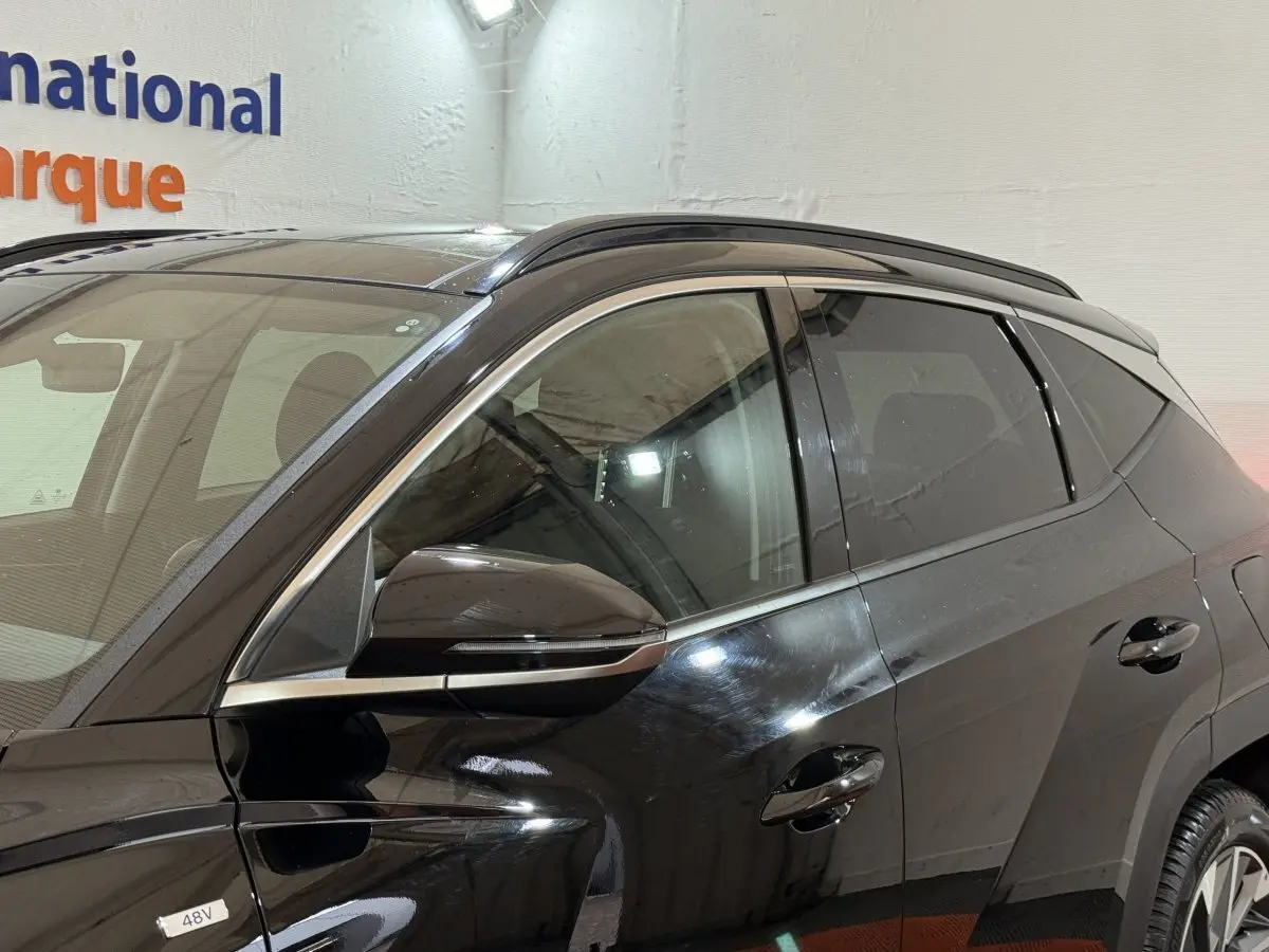 Vue latérale côté gauche d'un Hyundai Tucson noir 2021 avec rétroviseur et vitres teintées visibles.