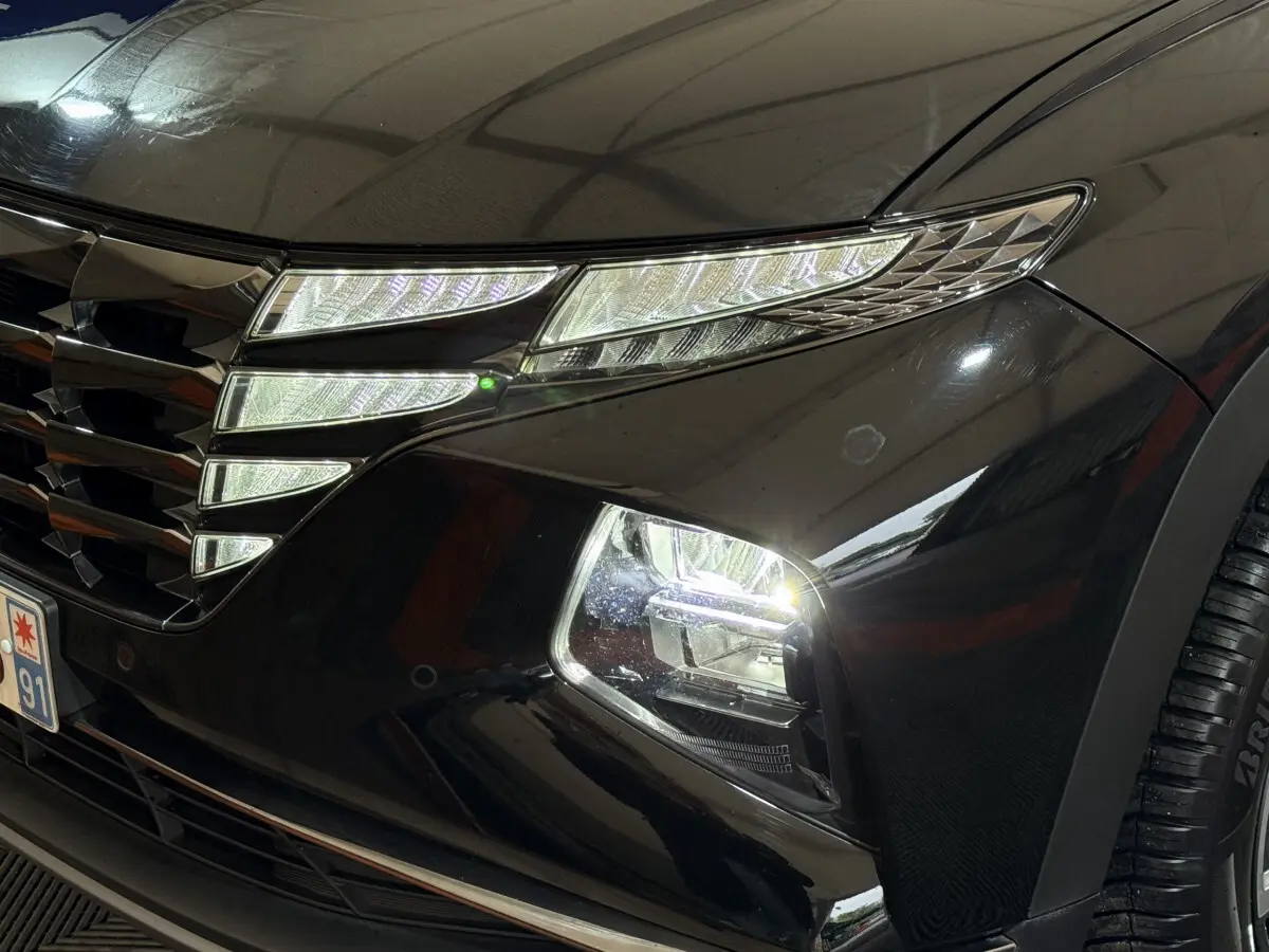 Gros plan sur le phare avant droit allumé d'un Hyundai Tucson noir, mettant en valeur la calandre et les LED distinctives.