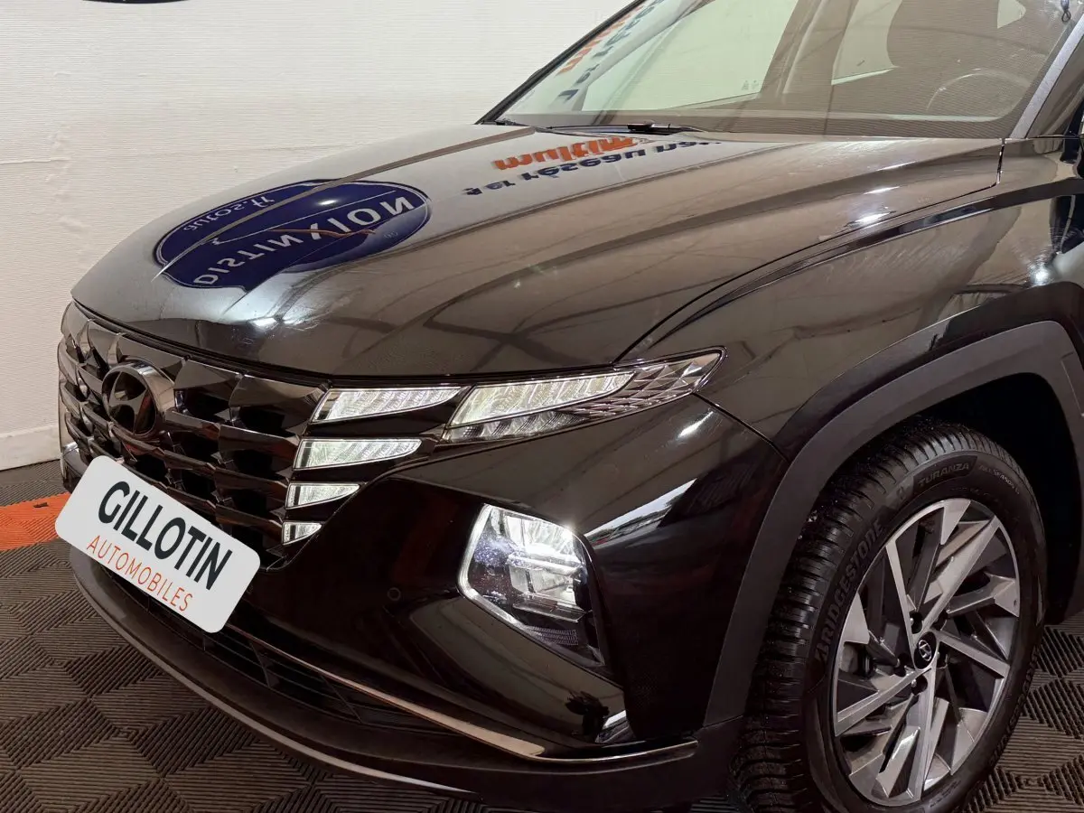 Vue 3/4 avant droite du Hyundai Tucson noir avec calandre distinctive et phares LED allumés.