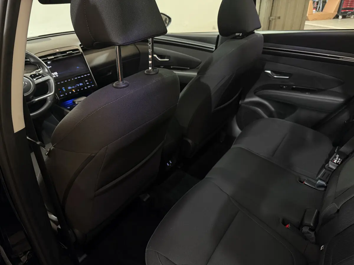 Intérieur noir du Hyundai Tucson 2021 vu depuis la porte arrière gauche, montrant les sièges arrière et le tableau de bord avant.