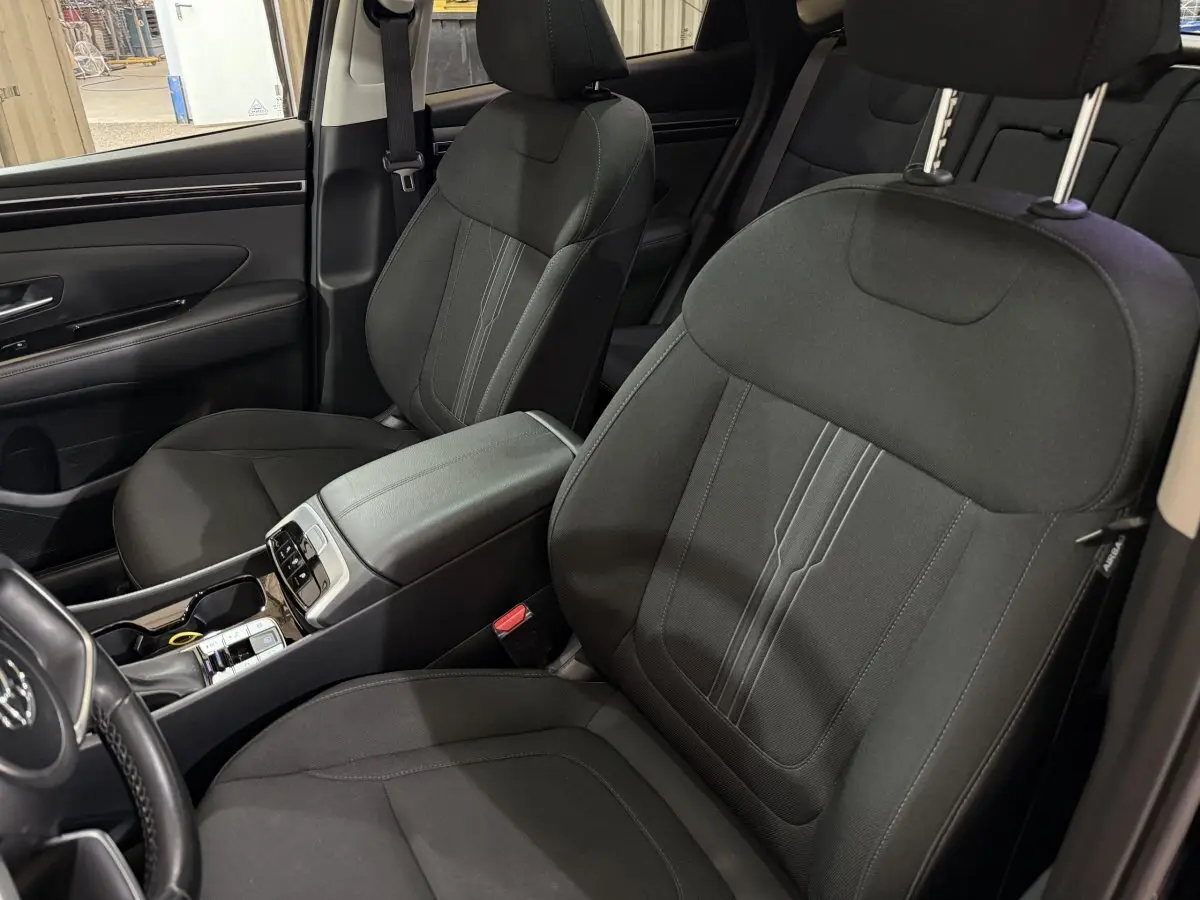 Vue intérieure côté avant gauche du Hyundai Tucson 2021, sièges noirs en tissu et console centrale avec commandes.