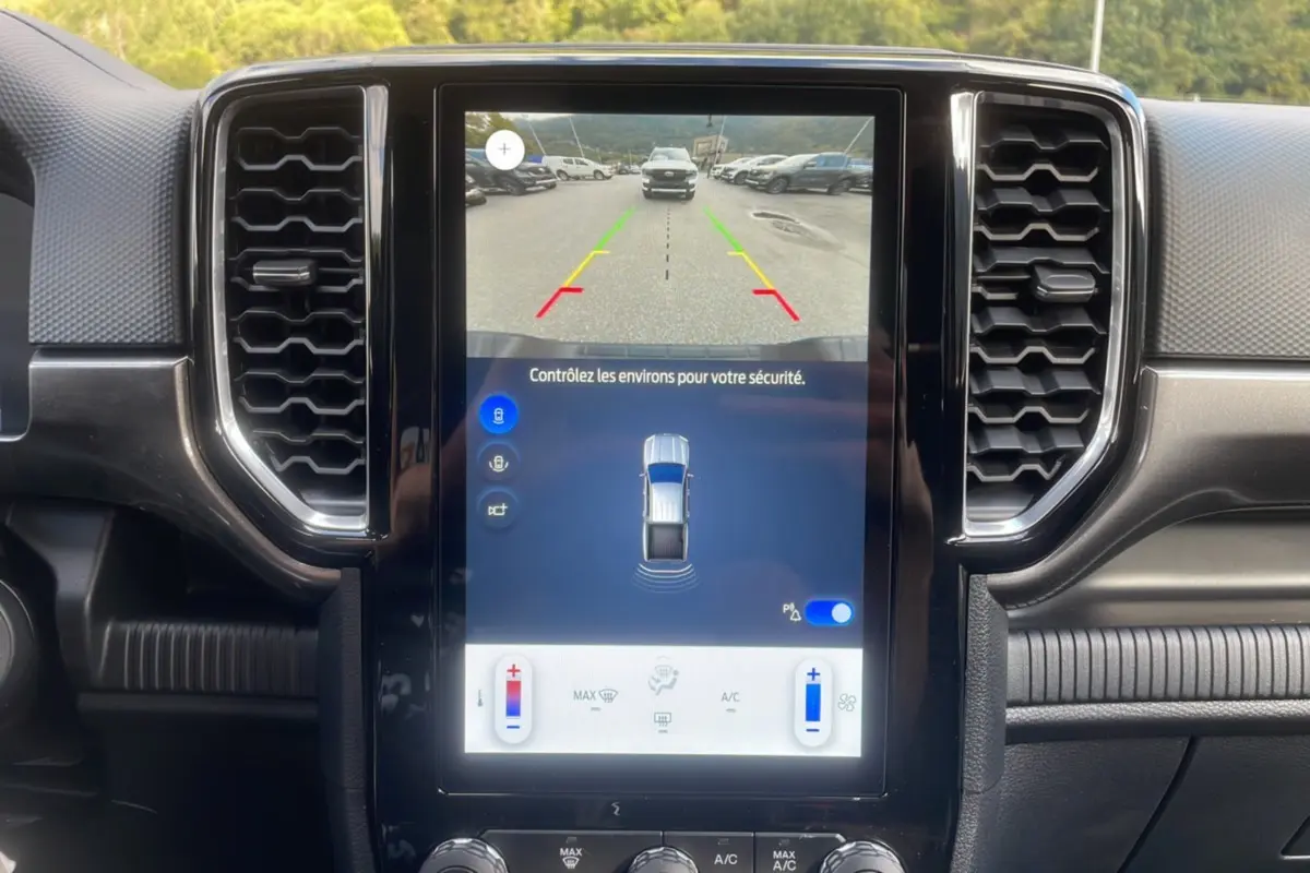 Vue du tableau de bord du Ford Ranger 2025 avec écran central tactile affichant caméra de recul et commandes climatisation.