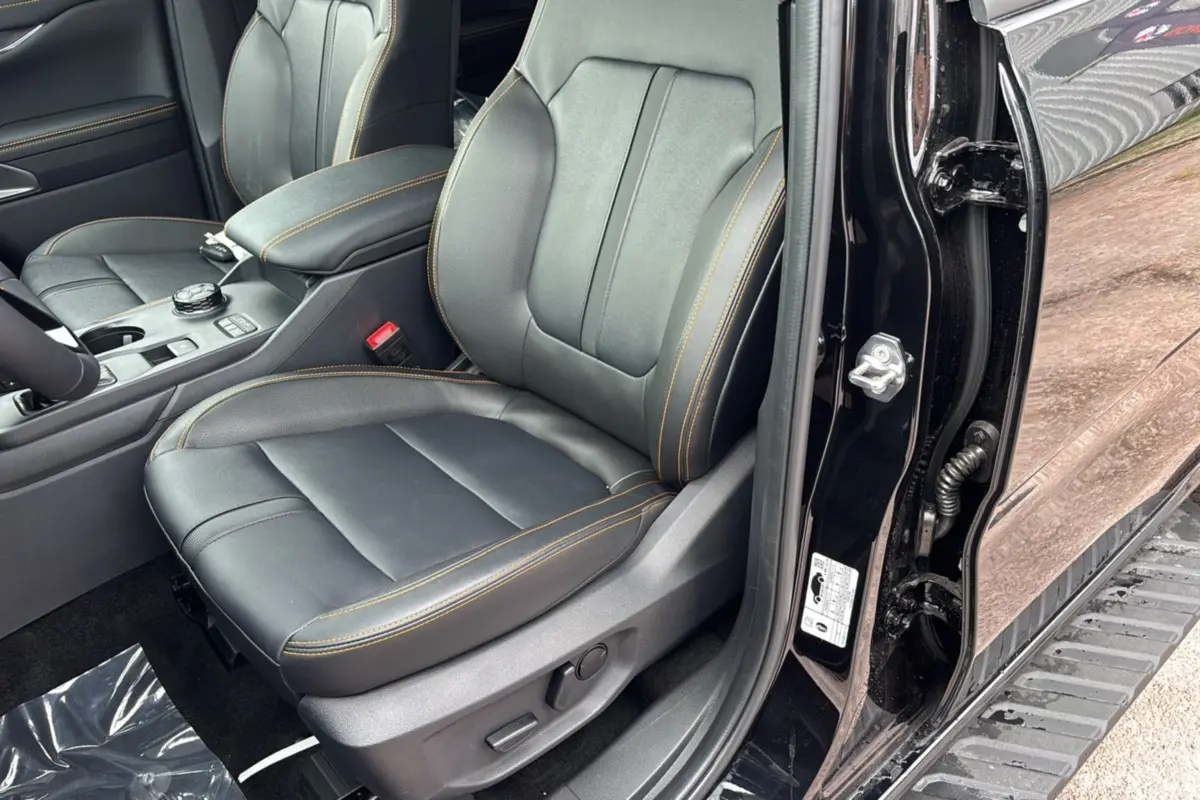 Vue intérieure côté conducteur du Ford Ranger 2025 noir agate, siège en cuir avec surpiqûres orange et console centrale visible.