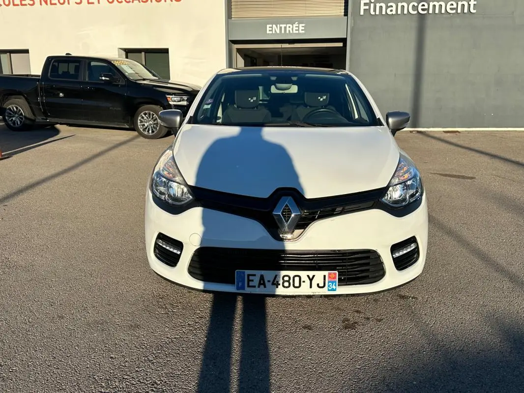 Renault Clio IV TCe 120 GT EDC blanc vue de face, avec calandre noire et feux avant allumés.