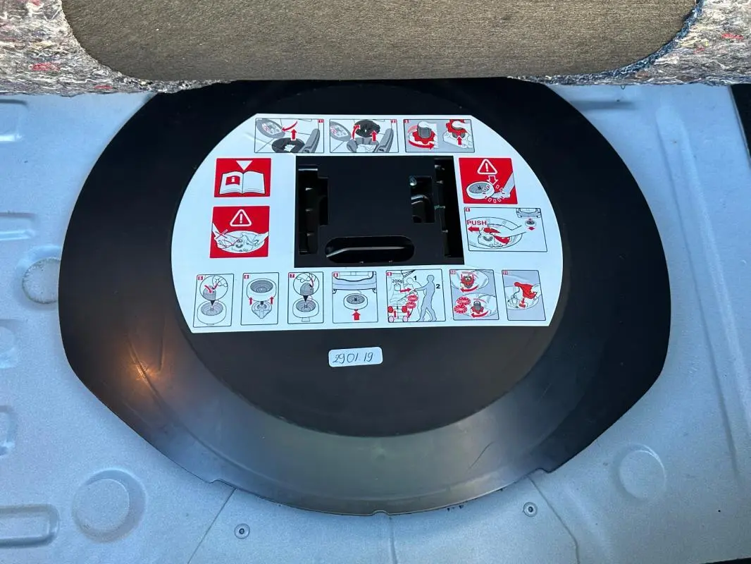 Gros plan sur la roue de secours noire avec instructions d'utilisation dans le coffre d'une Renault Clio IV blanche.