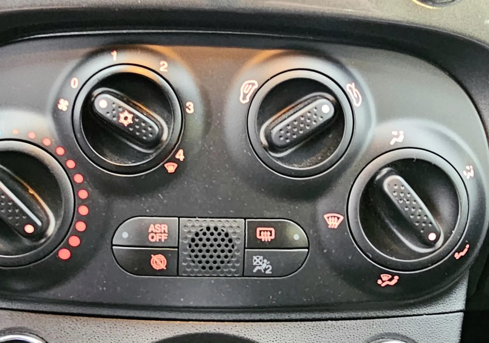 Panneau de commande de climatisation noir avec boutons rotatifs et indicateurs rouges et bleus dans une Fiat 500 gris 2023.