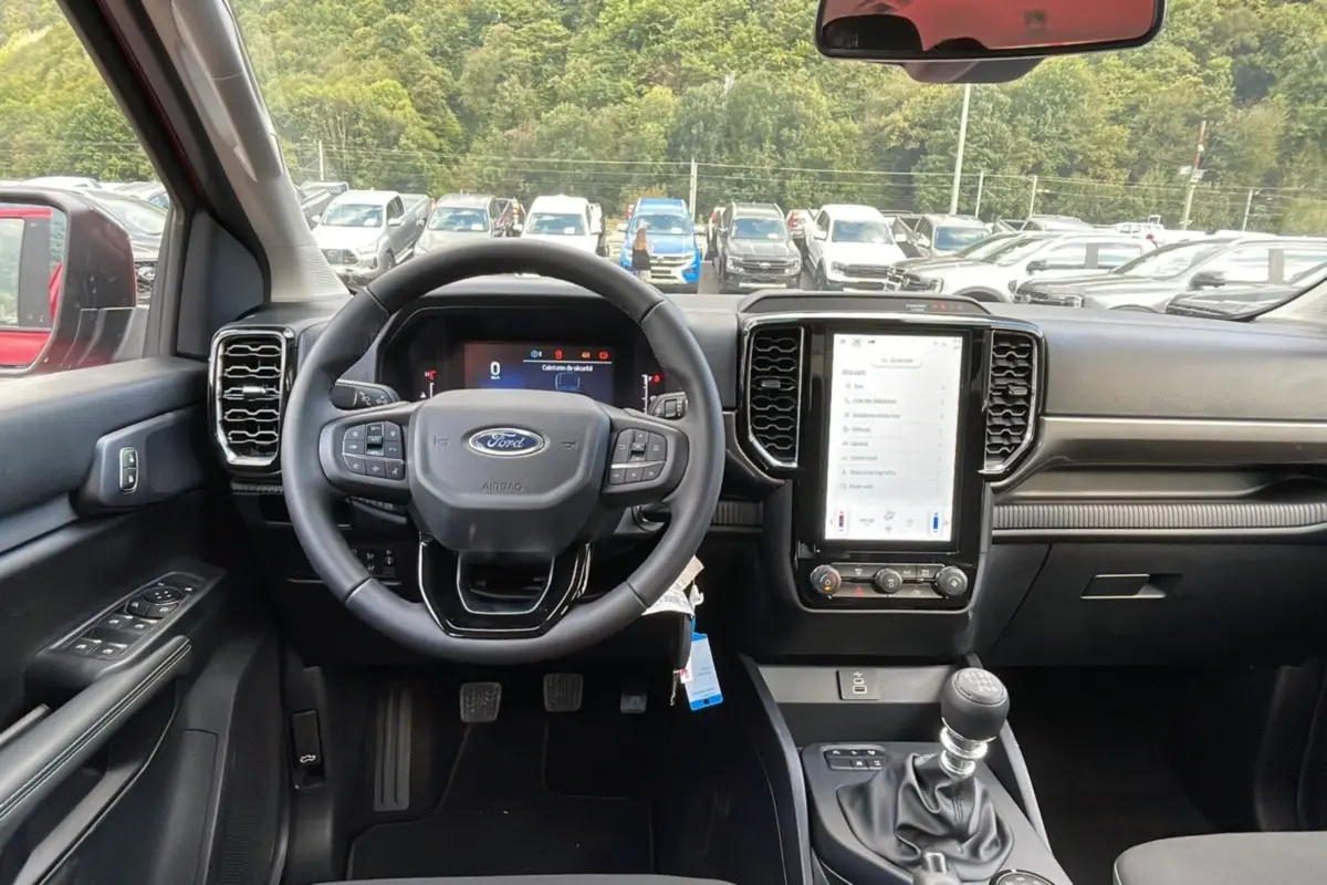 Vue intérieure centrée sur le volant et la console centrale du Ford Ranger rouge racing, avec boîte manuelle et écran tactile.