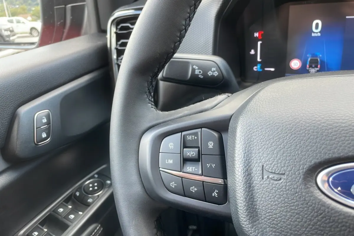 Gros plan sur le volant du Ford Ranger 2025 rouge racing, montrant les commandes multifonctions côté gauche et tableau de bord numérique.