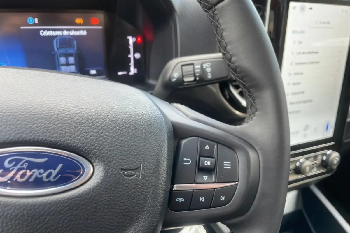 Vue rapprochée du volant cuir du Ford Ranger rouge 2025 avec commandes multifonctions et tableau de bord digital.