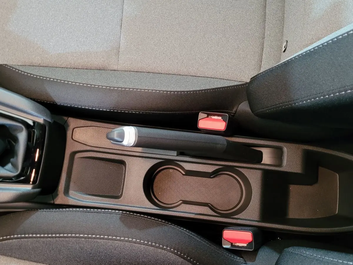 Vue en plongée sur la console centrale noire de la Renault Clio Evolution Blue dCi 100 avec frein à main manuel et porte-gobelets.