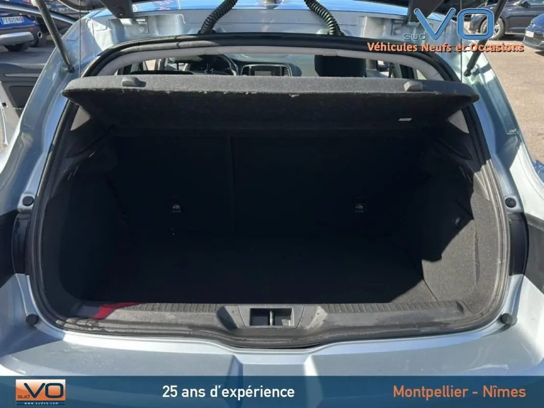 Coffre ouvert vu de l'arrière d'une Renault Mégane IV berline gris clair, montrant l'espace de chargement vide.